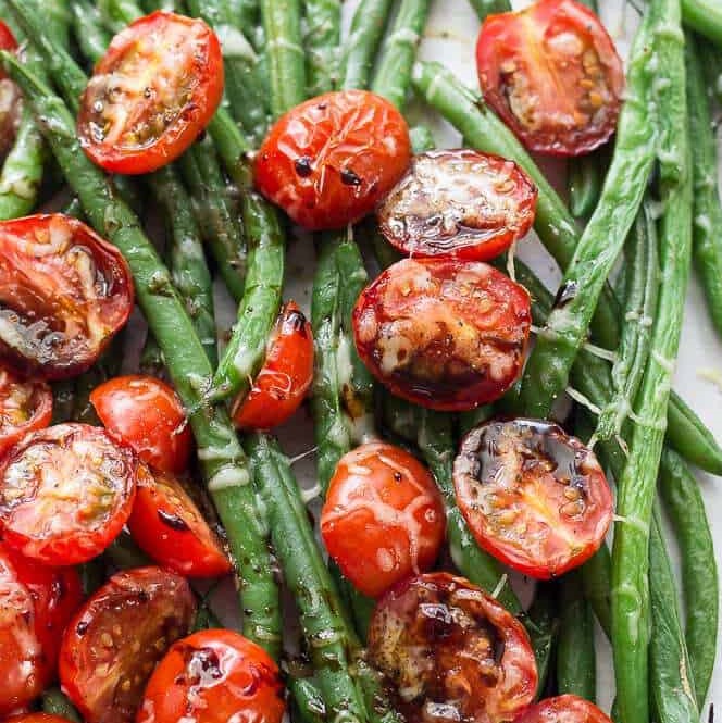Roasted green beans and halved cherry tomatoes, slightly browned and shiny with oil