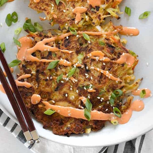 cabbage pancake drizzled with sriracha mayo on wite dish with brown chopsticks on side