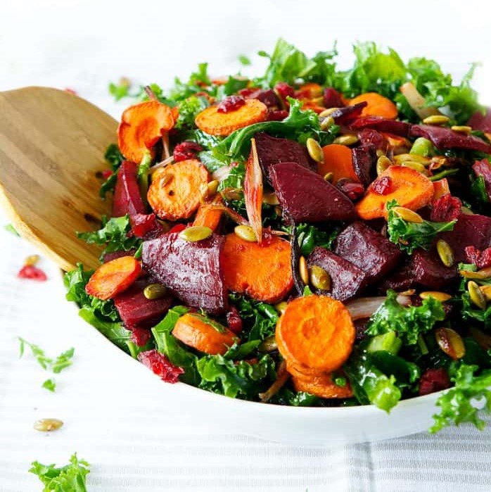 white bowl overflowing with massaged kale, roasted carrot, beetroot