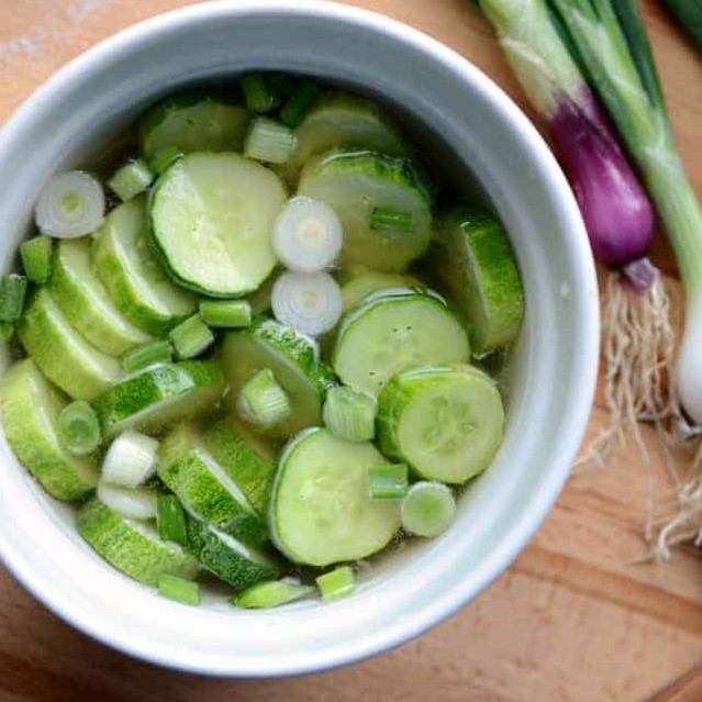 White bowl with sliced cucumbers and green onions in brine