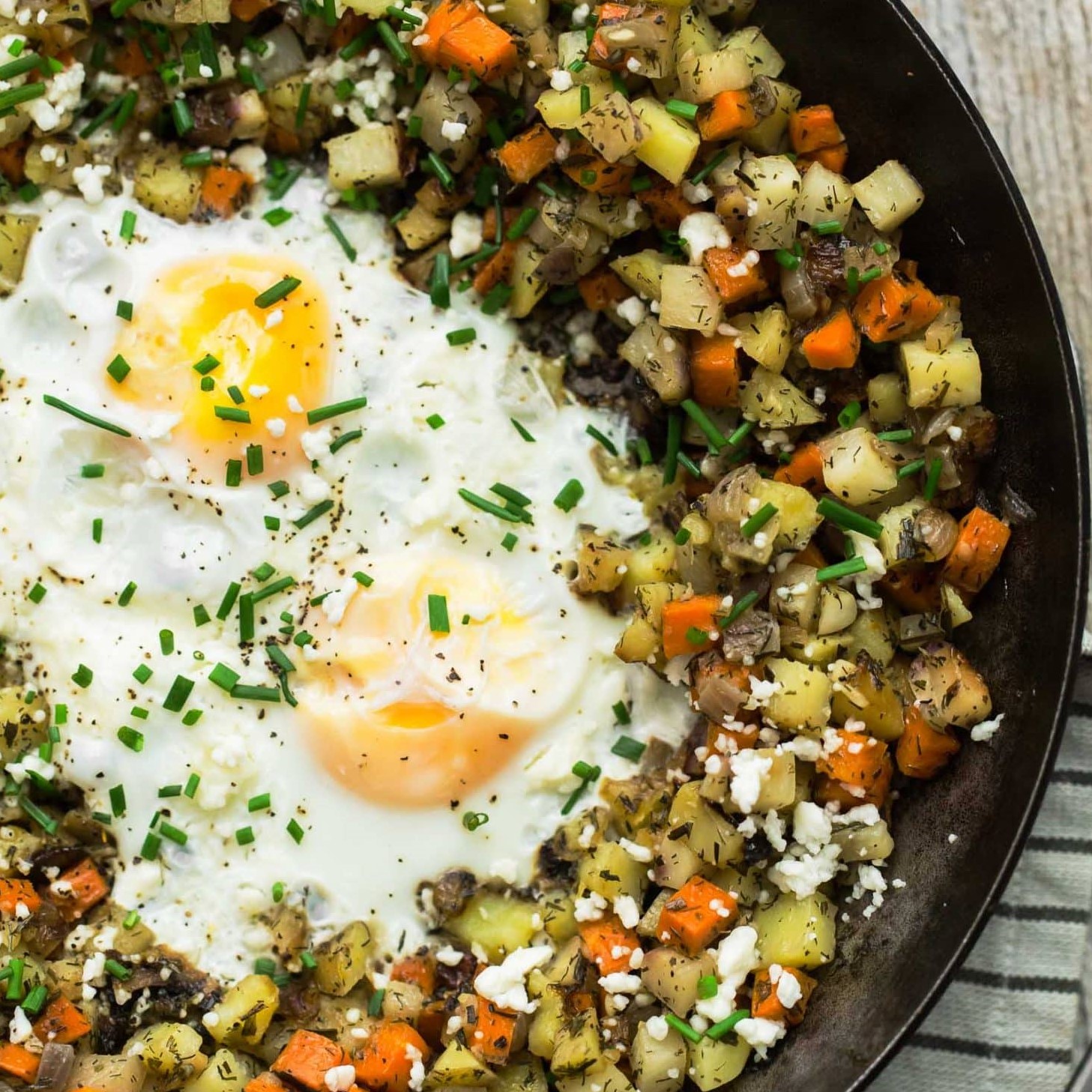close-up of skillet with finely diced root veggies, green herbs and friend egg in the middle
