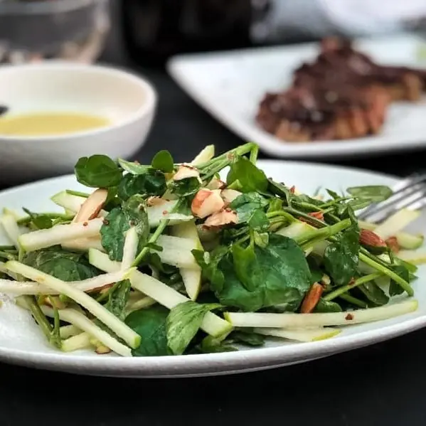 White plate with salad made from green watercress leaves, pear and apple cut in matchstick shapes and almonds