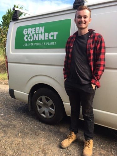 Young man in black with open red flannel shirt, standing in front of a white van with the Green Connect logo