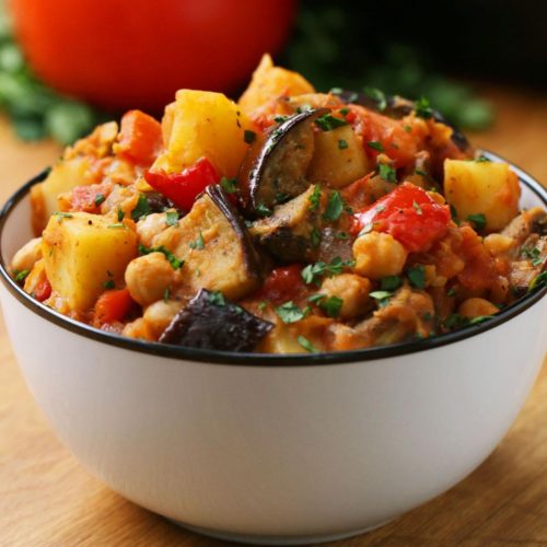White bowl with stew that has visible pieces of eggplants, tomatoes, potatoes, chickpeas and parsley