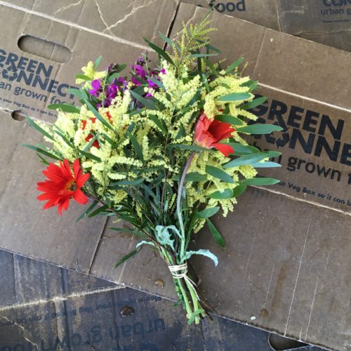Bouquet of yellow, red and purple flowers laying on flattened green connect veg boxes