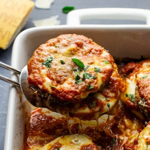Eggplant parmesan, with rich tomato sauce and melted cheese on top being lifted out of a baking dish