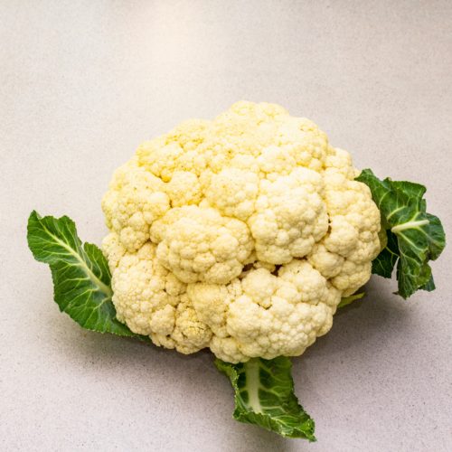 head of cauliflower with green leaves at base, white background