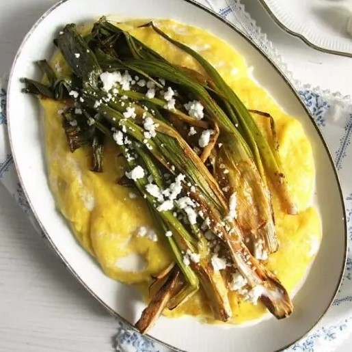 oval plate with creamy polenta topped with roasted spring onions with sprinkled feta on top